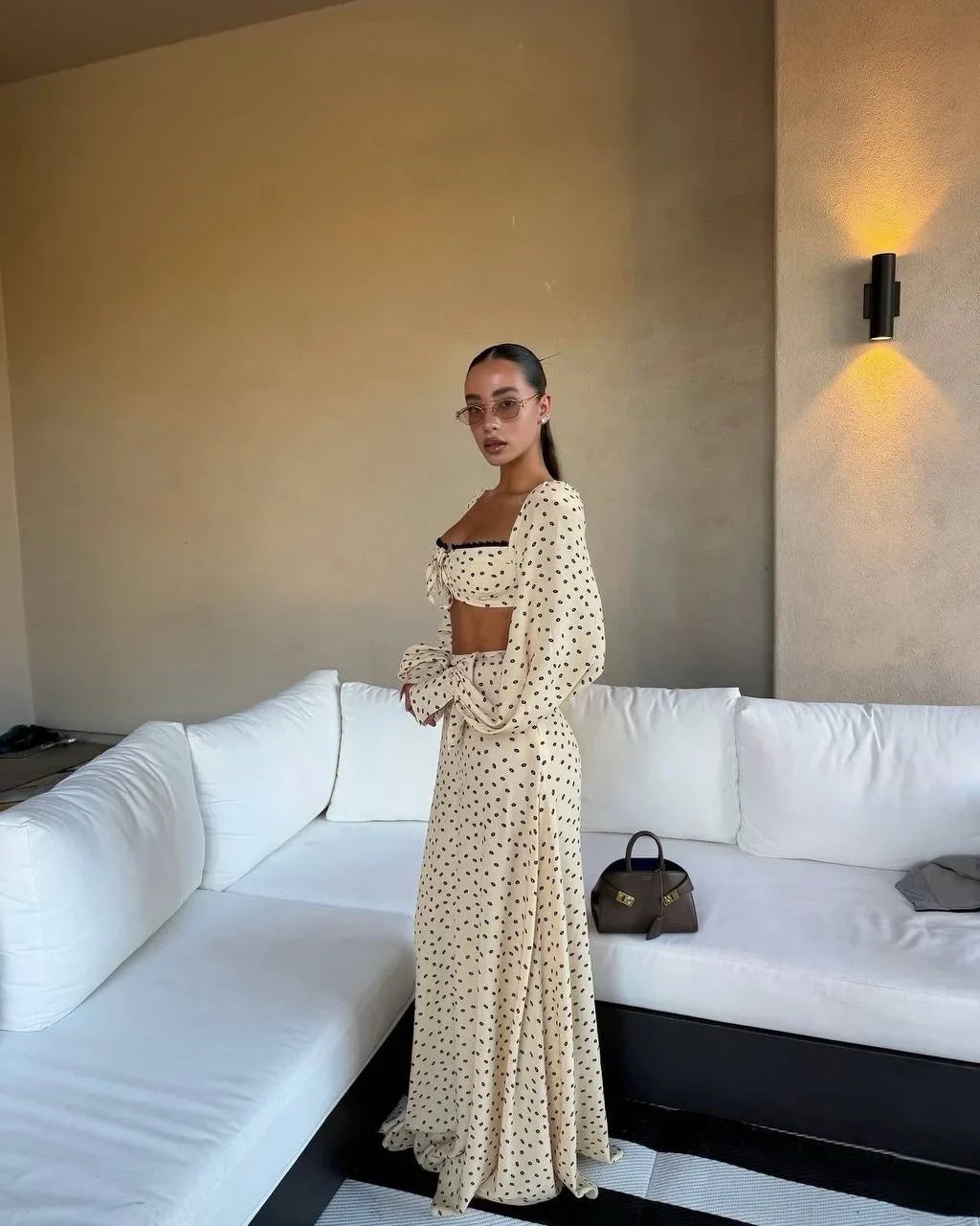 Woman in a polka dot dress standing in a room with a white couch and wall-mounted light fixture.